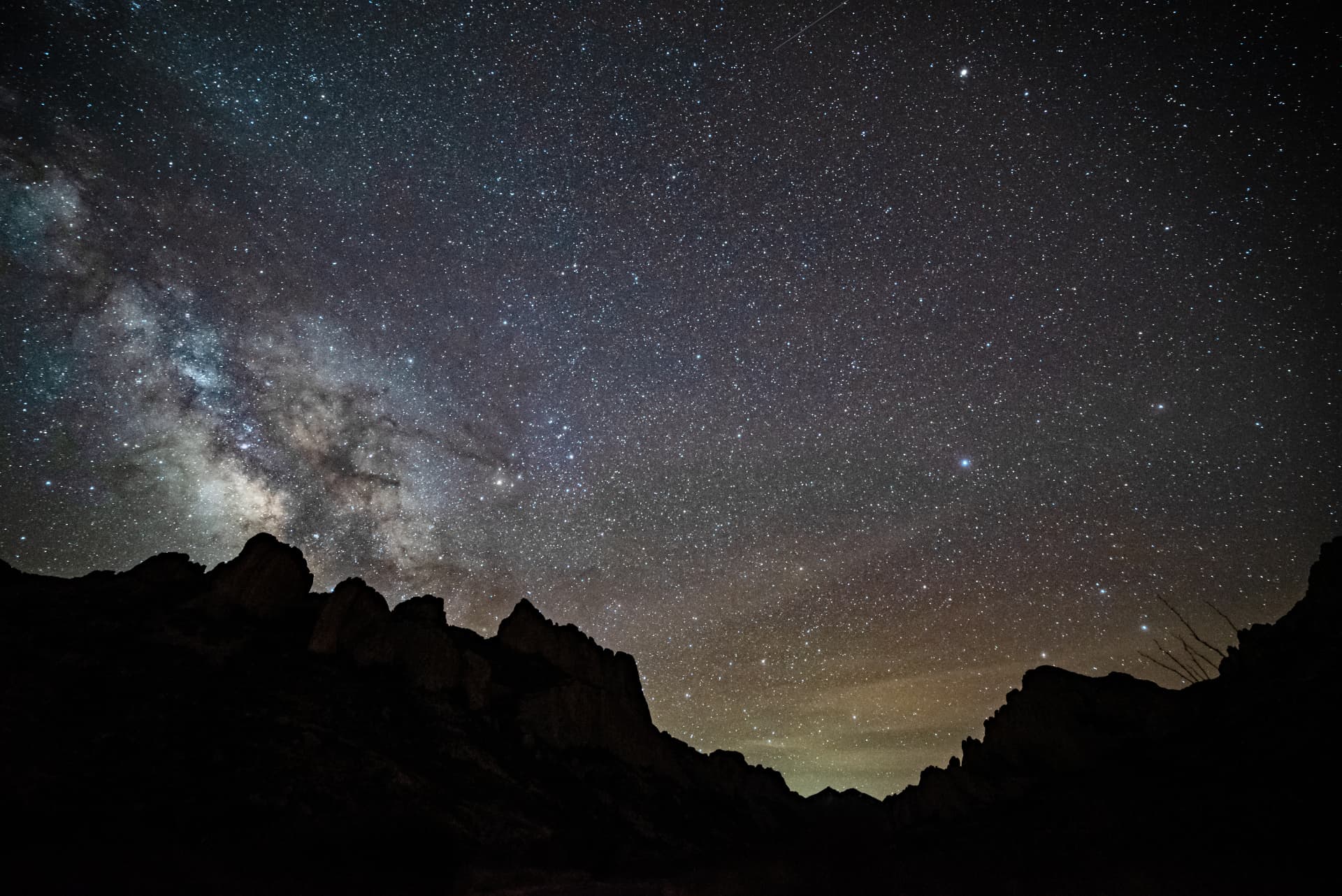 The Milky Way arching over desert yucca and a low mountain ridge on a moonless night
